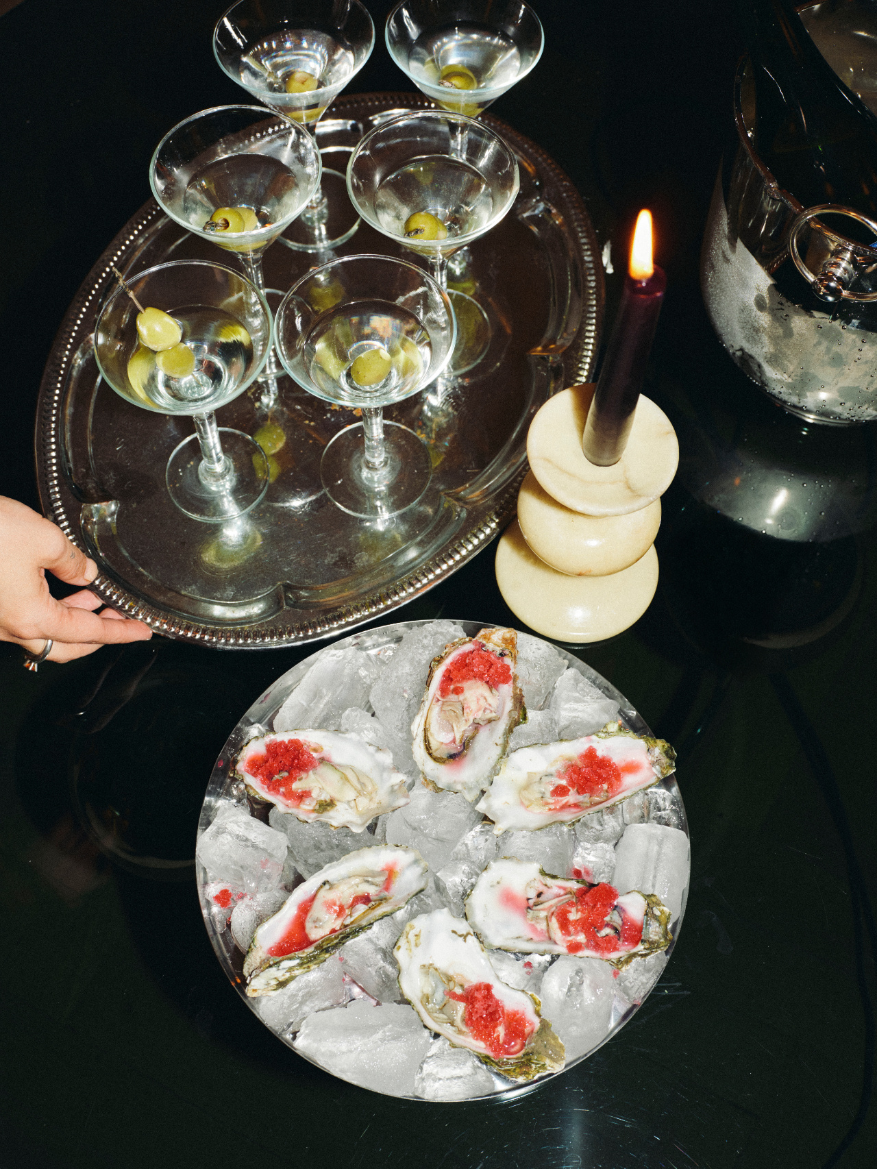 A silver tray of martinis beside oysters on ice by candlelight