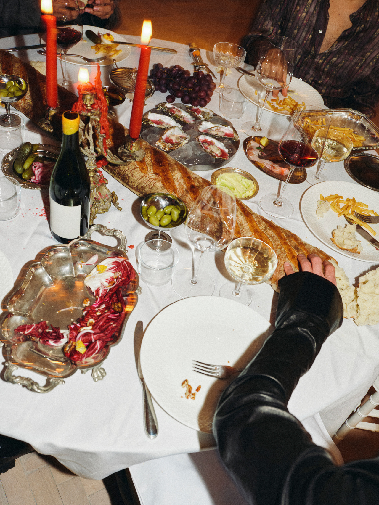 A candlelit dinner table mid-meal, guests talking over wine and shared plates